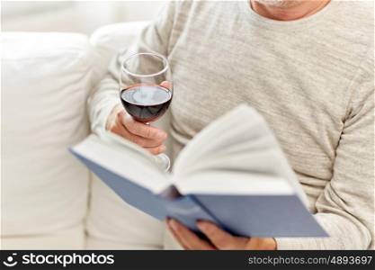 age, leisure and people concept - close up of senior man with wine glass reading book at home