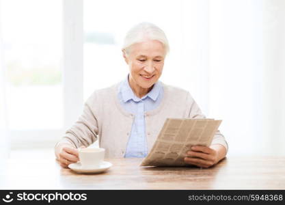 age, leisure and people concept - happy senior woman drinking coffee and reading newspaper at home