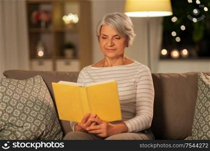 age, leisure and people concept - happy senior woman reading book at home in evening. happy senior woman reading book at home in evening