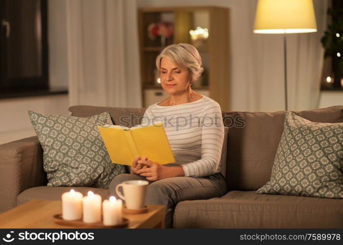 age, leisure and people concept - happy senior woman reading book at home in evening. happy senior woman reading book at home in evening