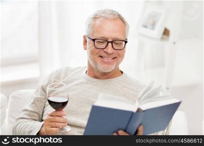 age, leisure and people concept - happy smiling senior man with wine glass reading book at home