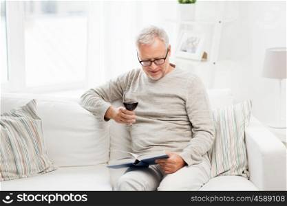age, leisure and people concept - happy smiling senior man with wine glass reading book at home