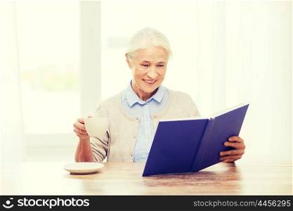 age, leisure and people concept - happy smiling senior woman drinking coffee and reading book at home