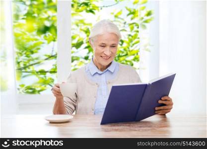 age, leisure and people concept - happy smiling senior woman drinking coffee and reading book at home over window and green natural background. happy smiling senior woman reading book at home