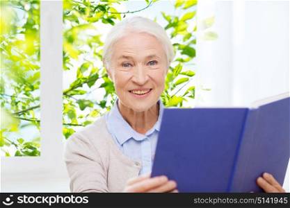 age, leisure and people concept - happy smiling senior woman reading book at home over window and green natural background. happy smiling senior woman reading book at home