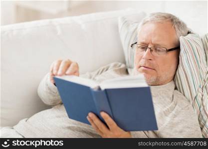 age, leisure and people concept - senior man lying on sofa and reading book at home