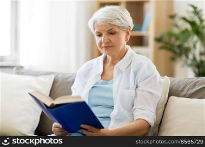 age, leisure and people concept - senior woman reading book at home. senior woman reading book at home
