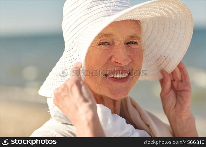 age, leisure, travel, tourism and people concept - close up of happy senior woman in sun hat on summer beach