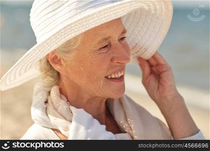age, leisure, travel, tourism and people concept - close up of happy senior woman in sun hat on summer beach