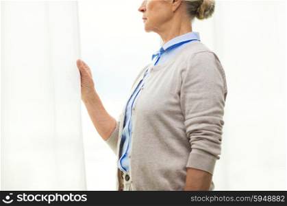 age, loneliness and people concept - close up of lonely senior woman looking through window at home
