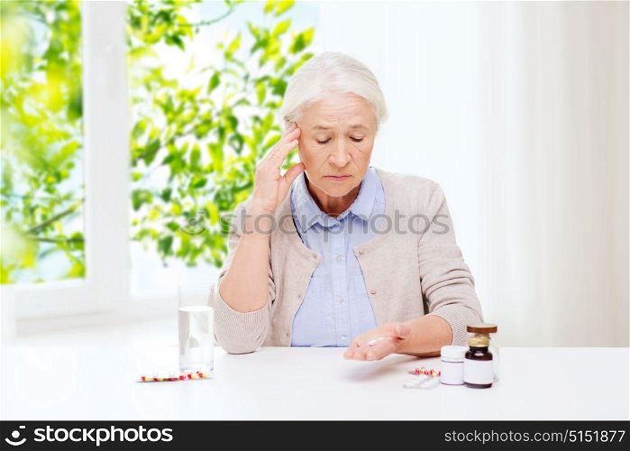 age, medicine and healthcare concept - senior woman with pills and glass of water at home over green natural background. senior woman with water and medicine at home