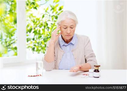 age, medicine and healthcare concept - senior woman with pills and glass of water at home over green natural background. senior woman with water and medicine at home