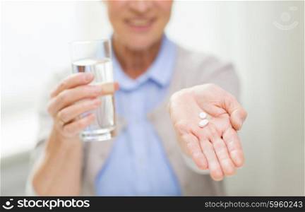 age, medicine, health care and people concept - close up of happy senior woman with pills and glass of water at home