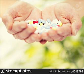age, medicine, health care and people concept - close up of senior woman cupped hands with pills over green natural background