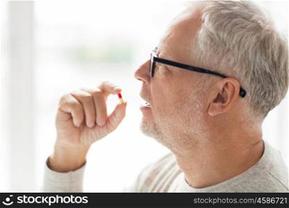 age, medicine, health care and people concept - close up of senior man taking medicine pill at home