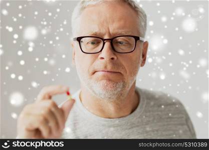 age, medicine, health care and people concept - close up of senior man taking pill at home over snow. close up of senior man taking medicine pill