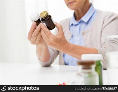 age, medicine, health care and people concept - close up of senior woman looking at jars with medicine at home or hospital office