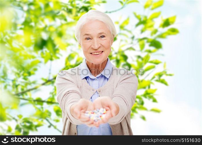 age, medicine, health care and people concept - happy senior woman with pills over green natural background. happy senior woman with medicine at home