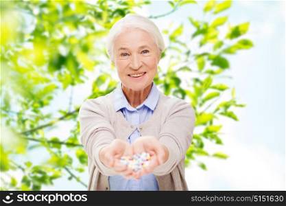 age, medicine, health care and people concept - happy senior woman with pills over green natural background. happy senior woman with medicine at home
