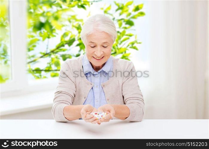 age, medicine, health care and people concept - happy senior woman with pills at home over green natural background. happy senior woman with medicine at home