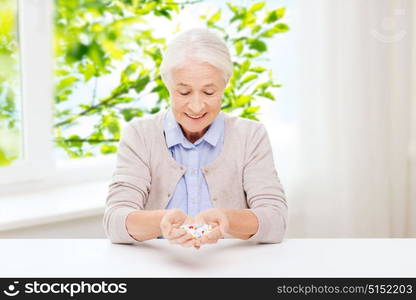 age, medicine, health care and people concept - happy senior woman with pills at home over green natural background. happy senior woman with medicine at home