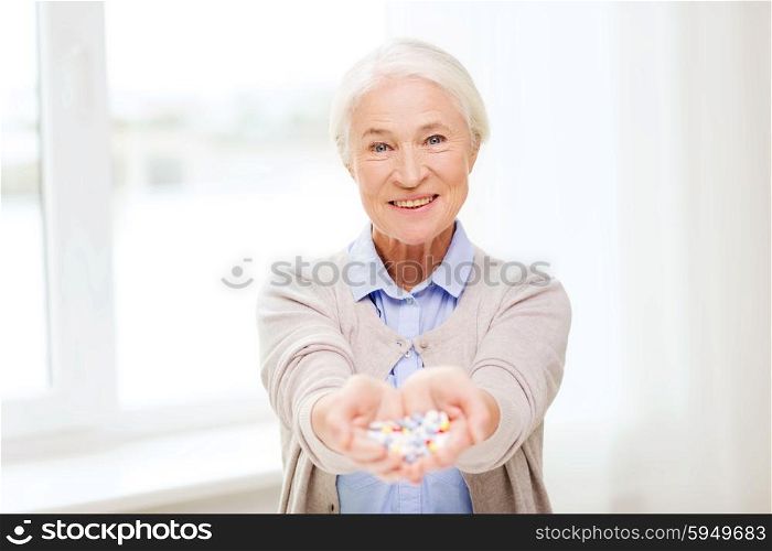 age, medicine, health care and people concept - happy senior woman with pills at home or hospital office