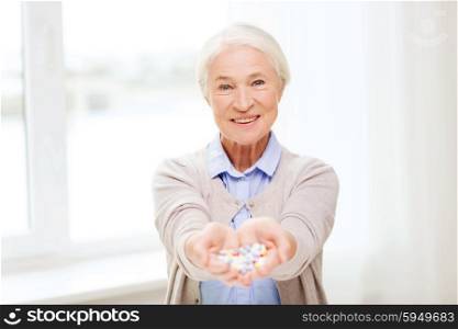age, medicine, health care and people concept - happy senior woman with pills at home or hospital office