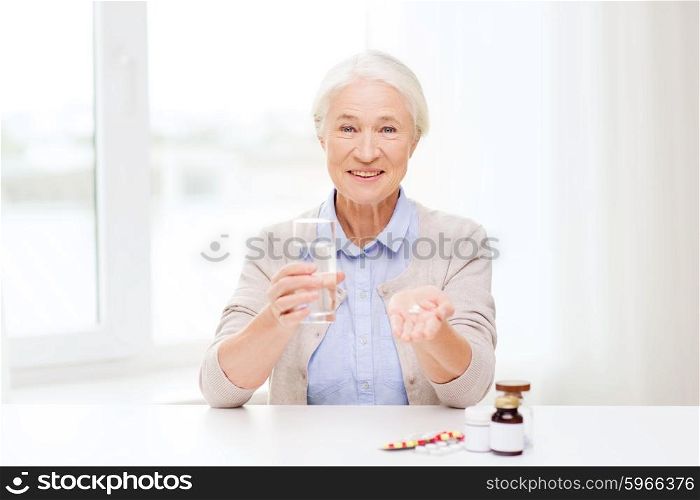 age, medicine, health care and people concept - happy senior woman with pills and glass of water at home