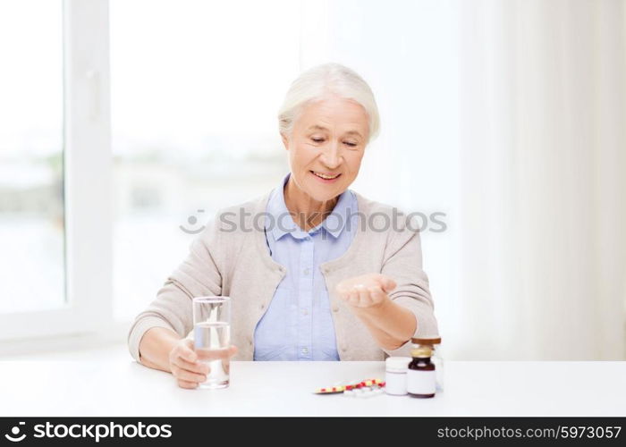 age, medicine, health care and people concept - happy senior woman with pills and glass of water at home