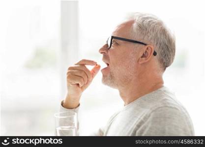 age, medicine, health care and people concept - senior man taking medicine pill at home