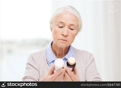age, medicine, health care and people concept - senior woman looking at jars with medicine at home or hospital office