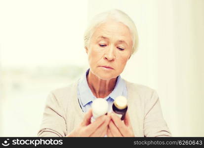 age, medicine, health care and people concept - senior woman looking at jars with medicine at home or hospital office