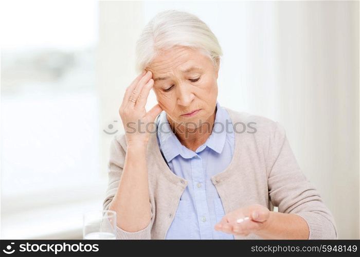 age, medicine, health care and people concept - senior woman with pills and glass of water at home