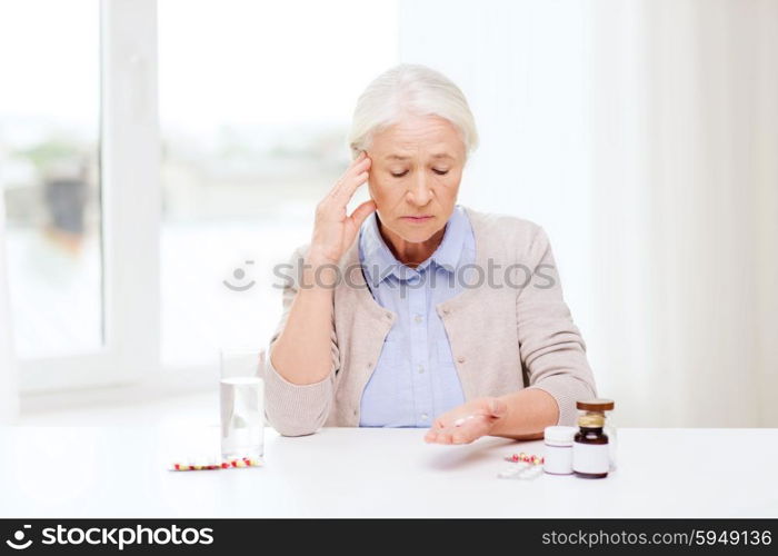 age, medicine, health care and people concept - senior woman with pills and glass of water at home