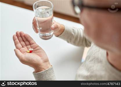 age, medicine, healthcare and people concept - close up of senior man hands with pills and water glass at home