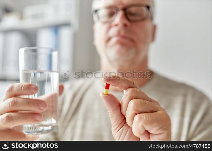 age, medicine, healthcare and people concept - close up of senior man hands with pill and water glass at home