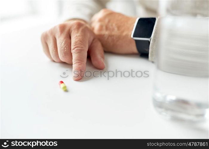 age, medicine, healthcare and people concept - close up of senior man hand with pill and smart watch
