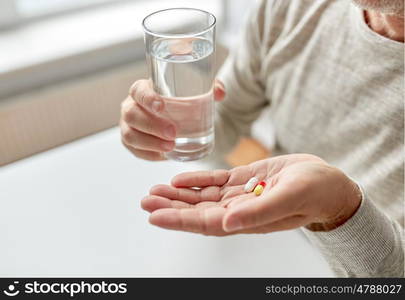 age, medicine, healthcare and people concept - close up of senior man hands with pills and water glass at home