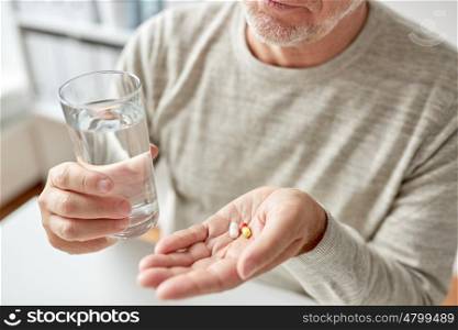 age, medicine, healthcare and people concept - close up of senior man hands with pills and water glass at home