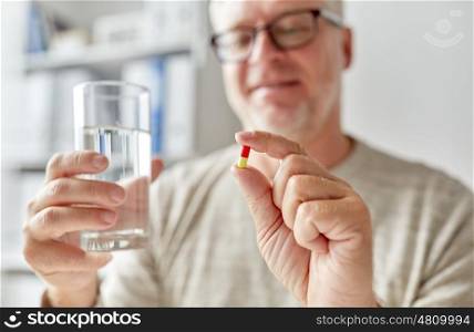 age, medicine, healthcare and people concept - close up of senior man hands with pill and water glass at home