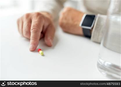age, medicine, healthcare and people concept - close up of senior man hand with pill and smart watch