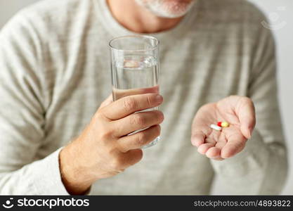 age, medicine, healthcare and people concept - close up of senior man hands with pills and water