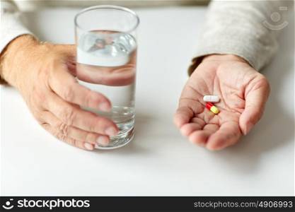 age, medicine, healthcare and people concept - close up of senior man hands with pills and water. close up of hands with medicine pills and water
