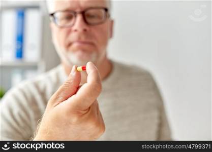 age, medicine, healthcare and people concept - close up of senior man hand with pill