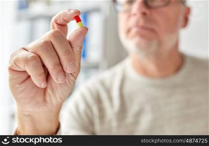 age, medicine, healthcare and people concept - close up of senior man hand with pill