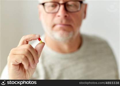 age, medicine, healthcare and people concept - close up of senior man with pill
