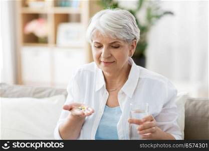 age, medicine, healthcare and people concept - senior woman with glass of water taking pills at home. senior woman with water taking medicine at home