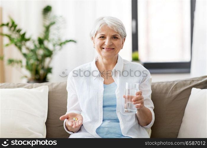 age, medicine, healthcare and people concept - senior woman with pills and glass of water at home. senior woman with water and medicine at home