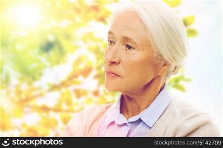 age, sadness and people concept - senior woman face over green natural background. senior woman face over green natural background