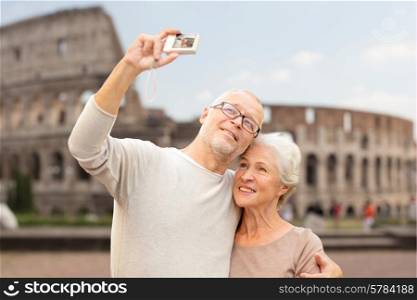 age, tourism, travel, technology and people concept - senior couple with camera taking selfie on street over coliseum background